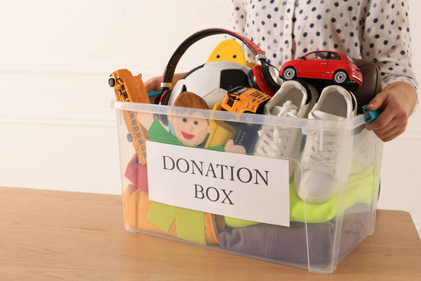 Woman holding donation box with child goods against light background, closeup - Foto, afbeelding