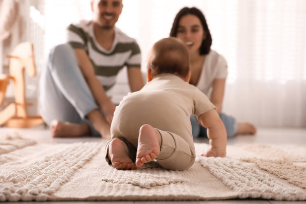 Happy parents watching their cute baby crawl on floor at home - Fotó, kép