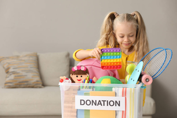 Cute little girl putting toy into donation box at home, space for text - Foto, immagini