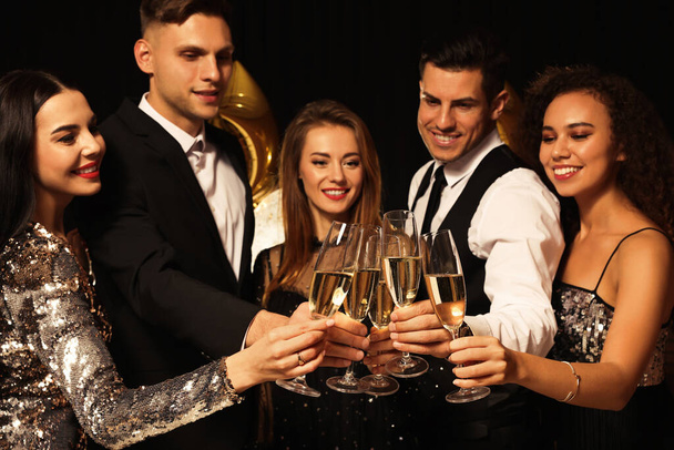 Happy friends with glasses of sparkling wine celebrating New Year on black background - Foto, Imagem