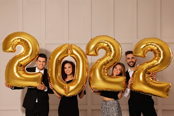 Happy friends with golden 2022 balloons indoors. New Year celebration - Photo, Image