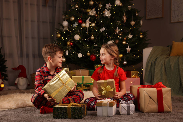 Cute little children with gift boxes near Christmas tree at home - Foto, Bild