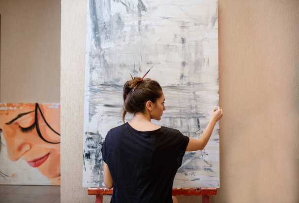 Back view of a young woman painter in her art studio paint an abstract picture with her brush - Photo, image