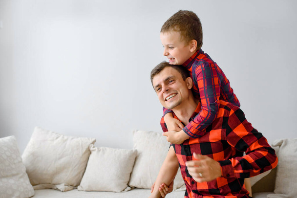 Смеющийся отец и его сын, в одних и тех же клетчатых рубашках играют и веселятся. Концепция счастливой семьи - Фото, изображение