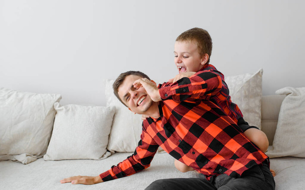 Naurava isä ja hänen poikansa, samoissa ruudullisissa paidoissa leikkivät ja pitävät hauskaa. Onnellinen perheen käsite - Valokuva, kuva