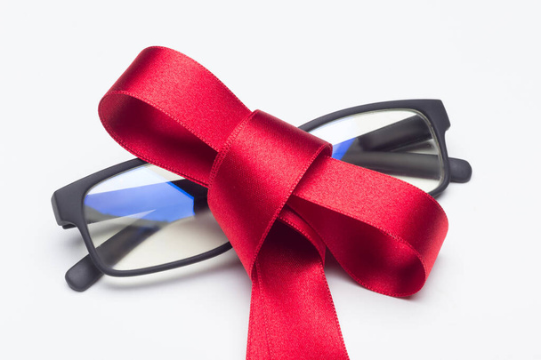 Μαύρα γυαλιά με κόκκινο φιόγκο για να δώσει ως δώρο σε λευκό φόντο - Φωτογραφία, εικόνα