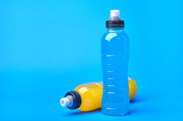 Standing and lying isotonic energy orange yellow and blue sport drink in plastic bottles on blue background - Fotó, kép