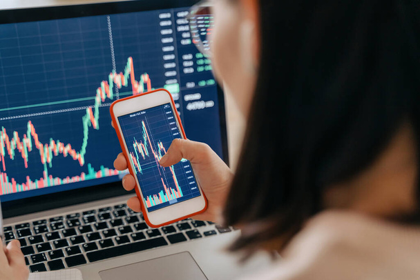 Nahaufnahme einer Aktienmarktanalystin, die eine Smartphone-Anlageapp hält, Wachstumsdiagramm mit Laptop für die Kryptowährung Finanzaktienmarktanalyse, Analyse von Graphenhandelsdaten - Foto, Bild