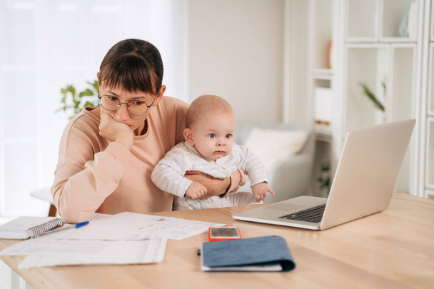 Young upset mother frustrated with financial problems, trying to find a solution while babysitting with her little child. Single unhappy mom looking at documents, tired of motherhood difficulties - Foto, Imagem