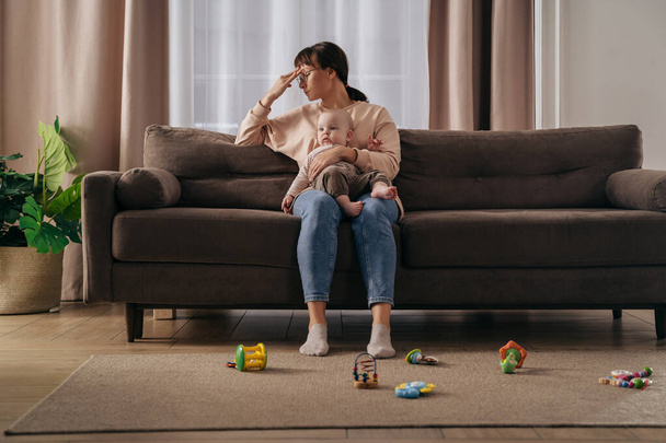Tired single mother suffering from postpartum depression. Exhausted frustrated woman holding her toddler baby on knees, feeling stressed with sleepless nights and stressful motherhood difficulties - Foto, Bild