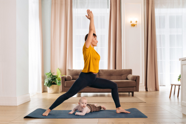 Postnatal recovery, sport for mom, happy motherhood. Healthy fit mom working out with her cute toddler baby on exercise mat at home. Smiling new mom practising yoga with her infant son, doing asana - Foto, immagini