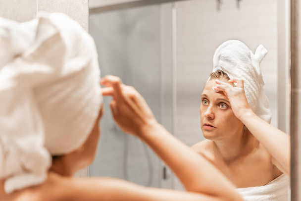 Donna adulta che applica crema idratante per la cura della pelle sulla fronte. - Foto, immagini
