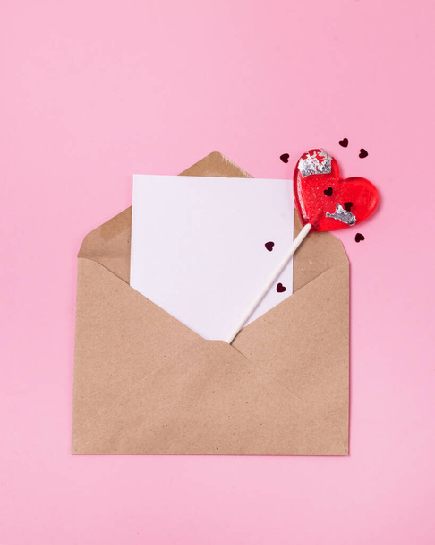 Mock up Valentines day concept Two red lollipop heart shape red confetti and Craft postal envelope on a pink background Minimal Top View - Foto, Imagen