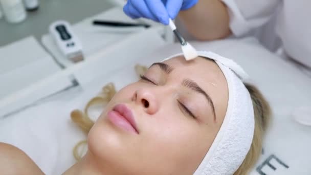 Beautician εφαρμογή προσώπου ξεφλούδισμα μάσκα με πινέλο. Γυναικεία διαδικασία δέρματος. Καλλυντικά εφαρμόζει λάδι στο πρόσωπο του πελάτη στο σαλόνι ομορφιάς - Πλάνα, βίντεο