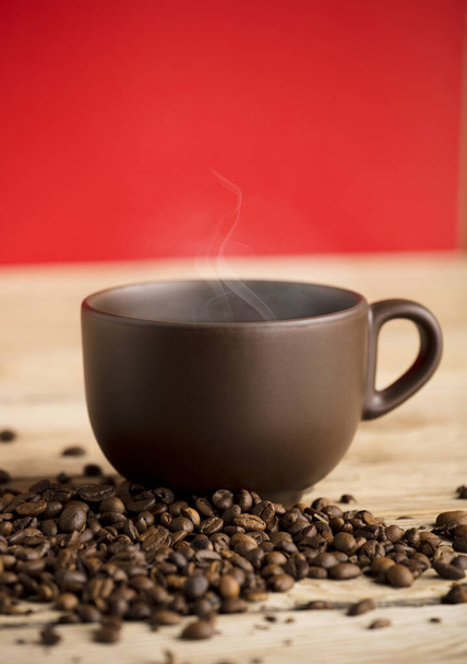 taza de café marrón con humo de vapor caliente y frijoles en la mesa de madera, fondo rojo - Foto, Imagen