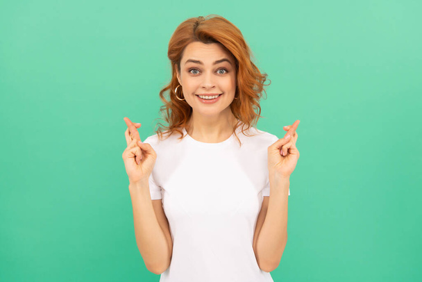 happy redhead woman with curly hair cross fingers making a wish on blue background, wish - Foto, Bild