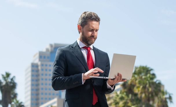 confident man in elegant suit checking email on pc outside, agile business - Photo, Image