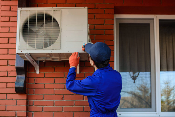 Jeune homme entrepreneur travailleur en salopette bleue et gants de protection sont la réparation ou l'installation de la climatisation - Photo, image