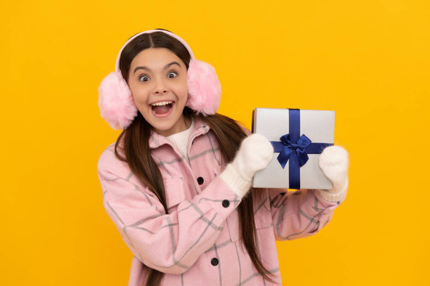 teen girl in mittens hold present on yellow background. xmas holiday gift. - Fotografie, Obrázek