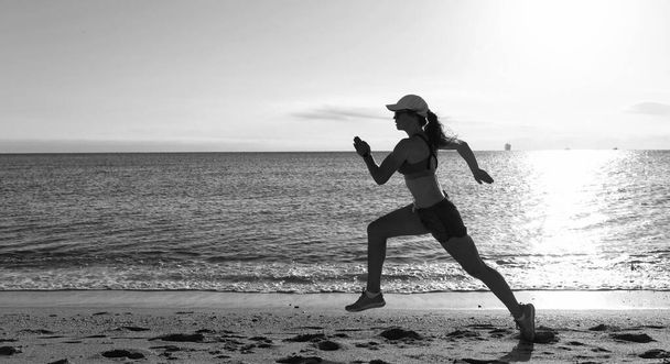 Hareketli giyimli enerjik bir kadın sahil kenarında kumsalda koşuyor. - Fotoğraf, Görsel