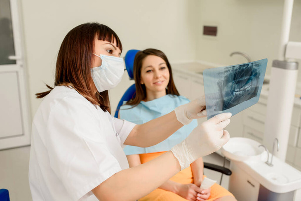 Jeune femme dentiste expliquant à sa patiente sur une radiographie dentaire panoramique tous les traitements dentaires qui doivent faire en dentisterie. Tenue de fil de radiographie dentaire - Photo, image