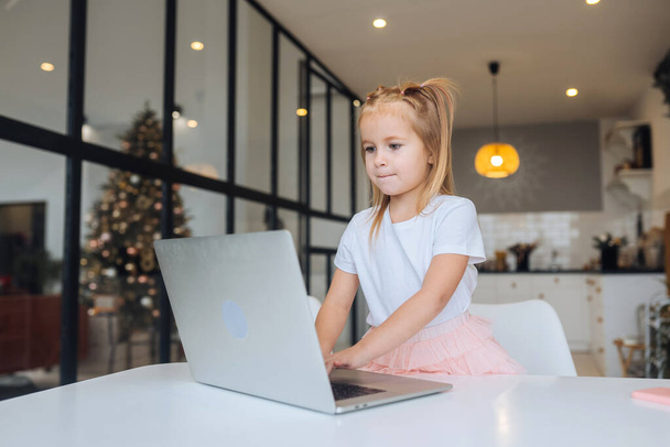 Маленькая девочка с планшетным компьютером сидит за столом - Фото, изображение