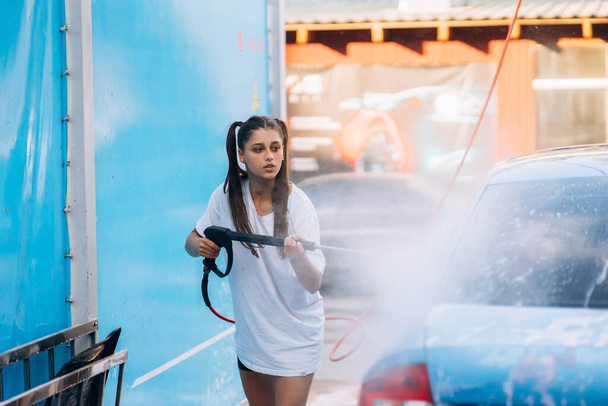 Brunette from a high-pressure hose washes the car at a car wash - Valokuva, kuva