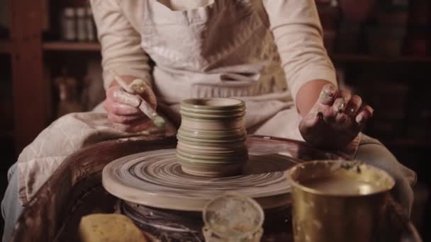 Young woman potter working with a wet clay - painting the clay in green color with a brush - Filmati, video