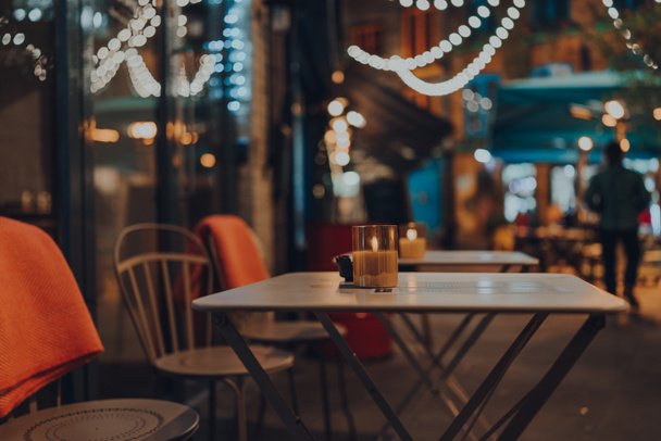 Encender la vela en una mesa al aire libre de un restaurante en invierno, luces de Navidad en el fondo, enfoque selectivo, bokeh. - Foto, imagen