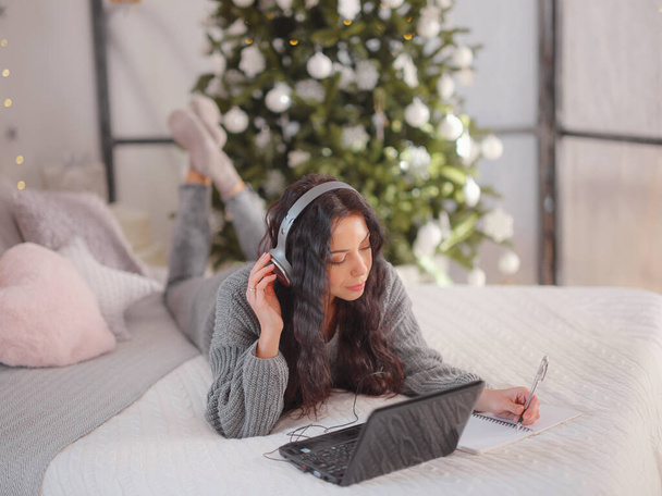 ベッドの上のラップトップを使用して居心地の良いグレーのニットセーターの女性,クリスマス休暇 - 写真・画像