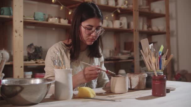 Mladá žena hrnčíř pracuje v ateliéru umění - dokončování finální keramický výrobek u stolu - Záběry, video