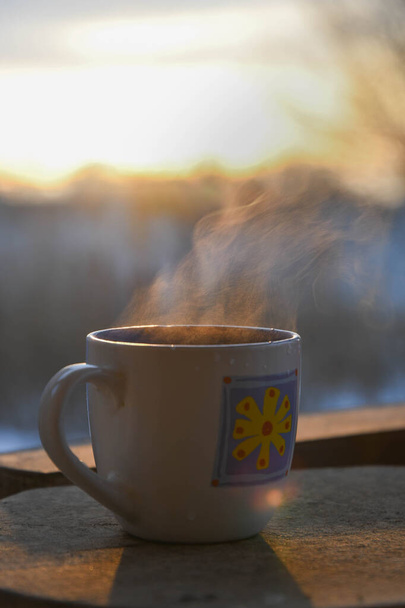 Aamukuppi kahvia talviterassilla nousevan auringon taustaa vasten. Auringonnousu. - Valokuva, kuva