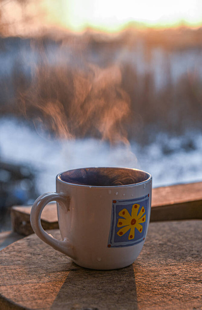 Aamukuppi kahvia talviterassilla nousevan auringon taustaa vasten. Auringonnousu. - Valokuva, kuva