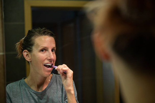 Отражение в зеркале ванной молодой женщины, чистящей зубы. - Фото, изображение