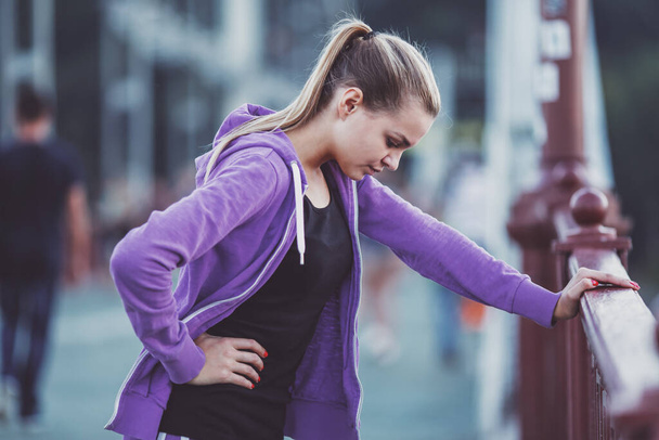 The young beautiful girl with headphones running and doing fitness in city - Photo, Image