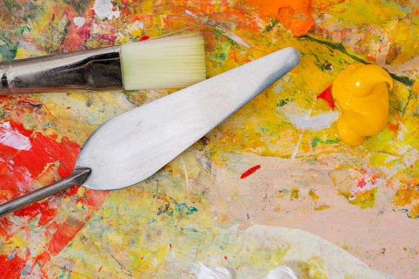 Detailní záběr umělecké palety s barevnými smíšenými barvami a paletovým nožem a štětcem. Koncept umění - Fotografie, Obrázek