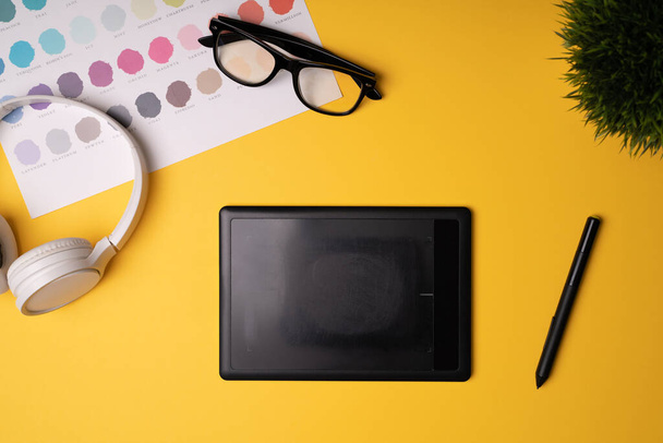 グラフィックタブレットとデジタル鉛筆。黄色の背景にヘッドフォンや眼鏡とグラフィックデザイナーのワークスペース  - 写真・画像
