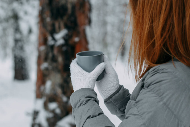 A man in the winter in the forest holds a gray mug with a hot drink in his hands. Warm and cozy in the winter park.selective focus. - Foto, immagini