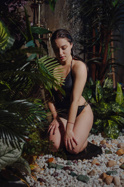 Woman in bikini sitting under tropical shower - 写真・画像