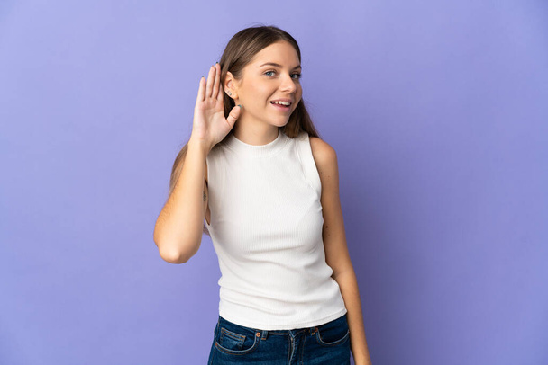 Young Lithuanian woman isolated on purple background listening to something by putting hand on the ear - Photo, Image