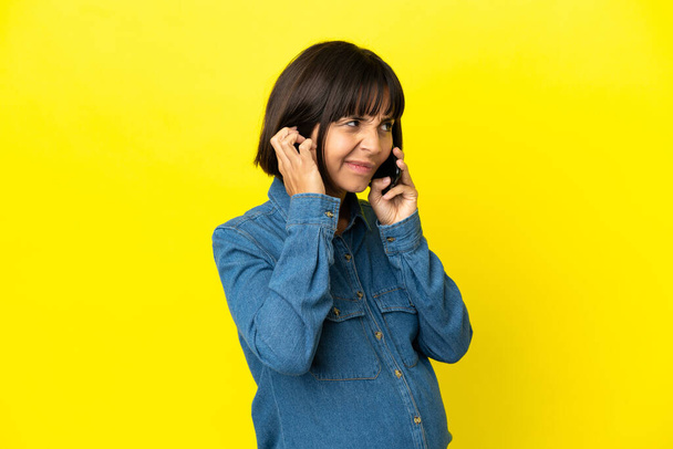 Pregnant woman using mobile phone isolated on yellow background frustrated and covering ears - Foto, Imagem