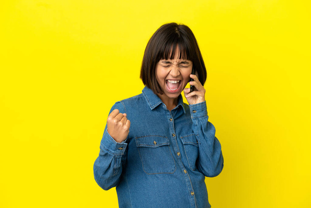 Pregnant woman using mobile phone isolated on yellow background celebrating a victory - Photo, Image