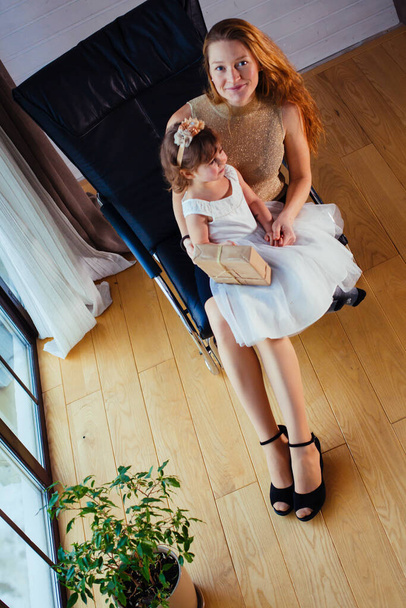 Fehér ruhás kislány szerető anyjával otthon ül a virágcserép mellett. - Fotó, kép
