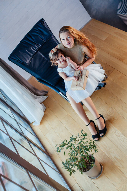 Beyaz elbiseli küçük bir kız ve sevgili annesi evde, saksının yanında oturuyor. - Fotoğraf, Görsel