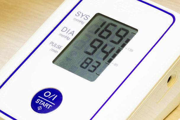 The digital blood pressure monitor shows very high arterial blood pressure and heart rate. Medical pressure measuring device. Diastolic and systolic pressure, heart rate pulse on the screen close-up. - Photo, Image
