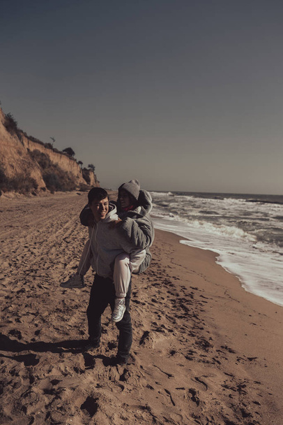 Hombre lleva a su novia en la espalda, pareja divirtiéndose en la orilla del mar - Foto, imagen