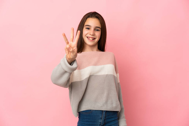 Petite fille isolée sur fond rose heureuse et comptant trois doigts - Photo, image