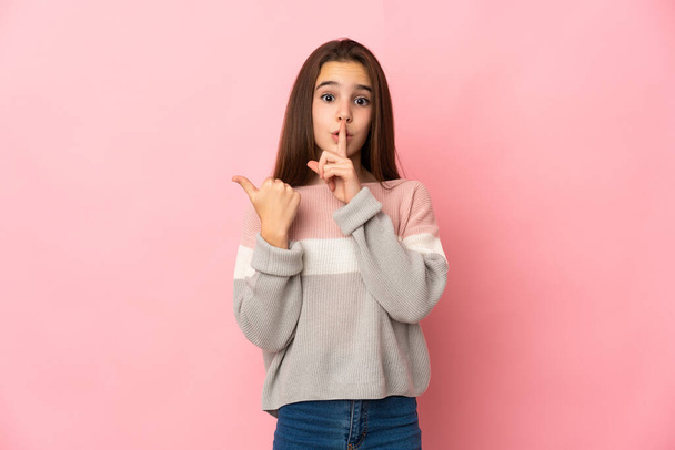 Little girl isolated on pink background pointing to the side and doing silence gesture - Photo, image