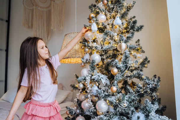 Adorable niña decorando un árbol de Navidad con bolas en casa
 - Foto, Imagen