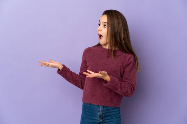 Little girl isolated on purple background with surprise expression while looking side - Photo, Image